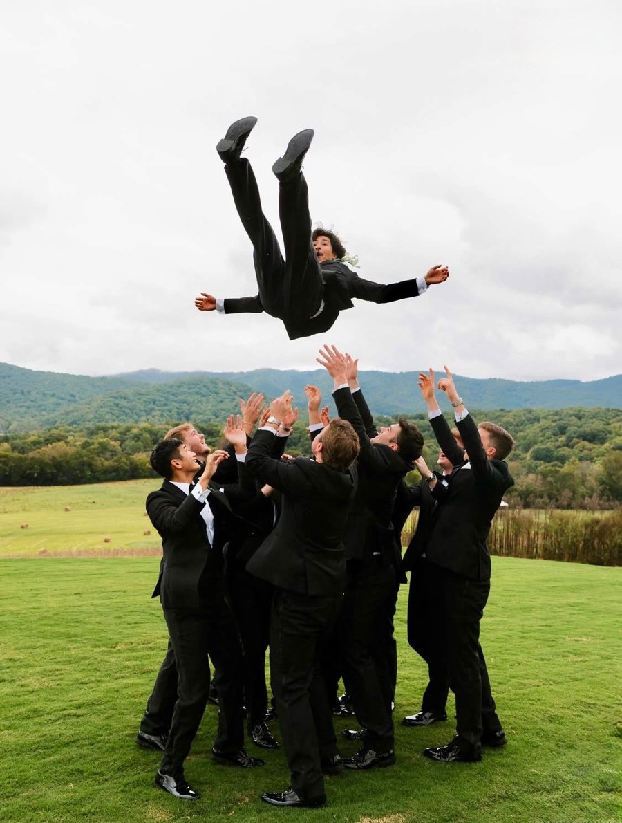 Groomsmen toss the groom into the air on the lawn, mountains behind them