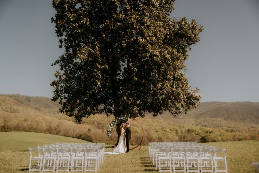 Ceremony chairs set on the crest beneath the tree, ridgelines beyond